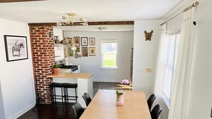 Un coin repas avec une table en bois, des chaises noires, un mur en briques servant de décoration, et une cuisine en arrière-plan.