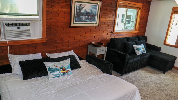 A bedroom with a bed, two black chairs, a small table, and a picture on the wall.
