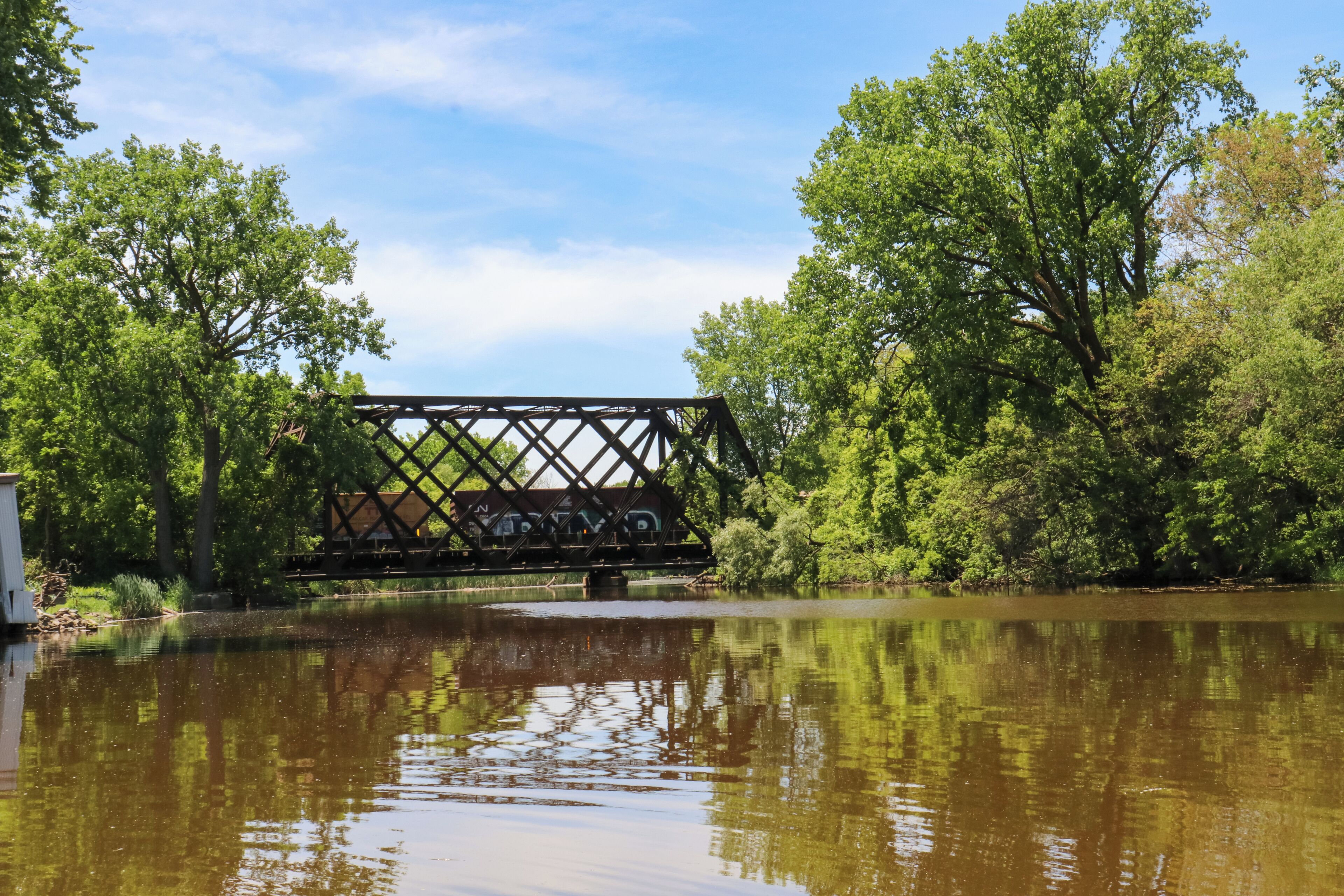 Un pont enjambant une rivière paisible, bordée d’arbres de chaque côté.