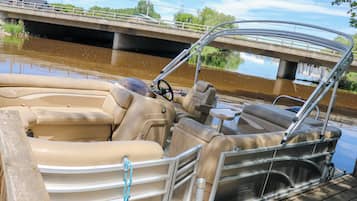 A pontoon boat docked at a pier with a metal railing and a view of a bridge in the background.