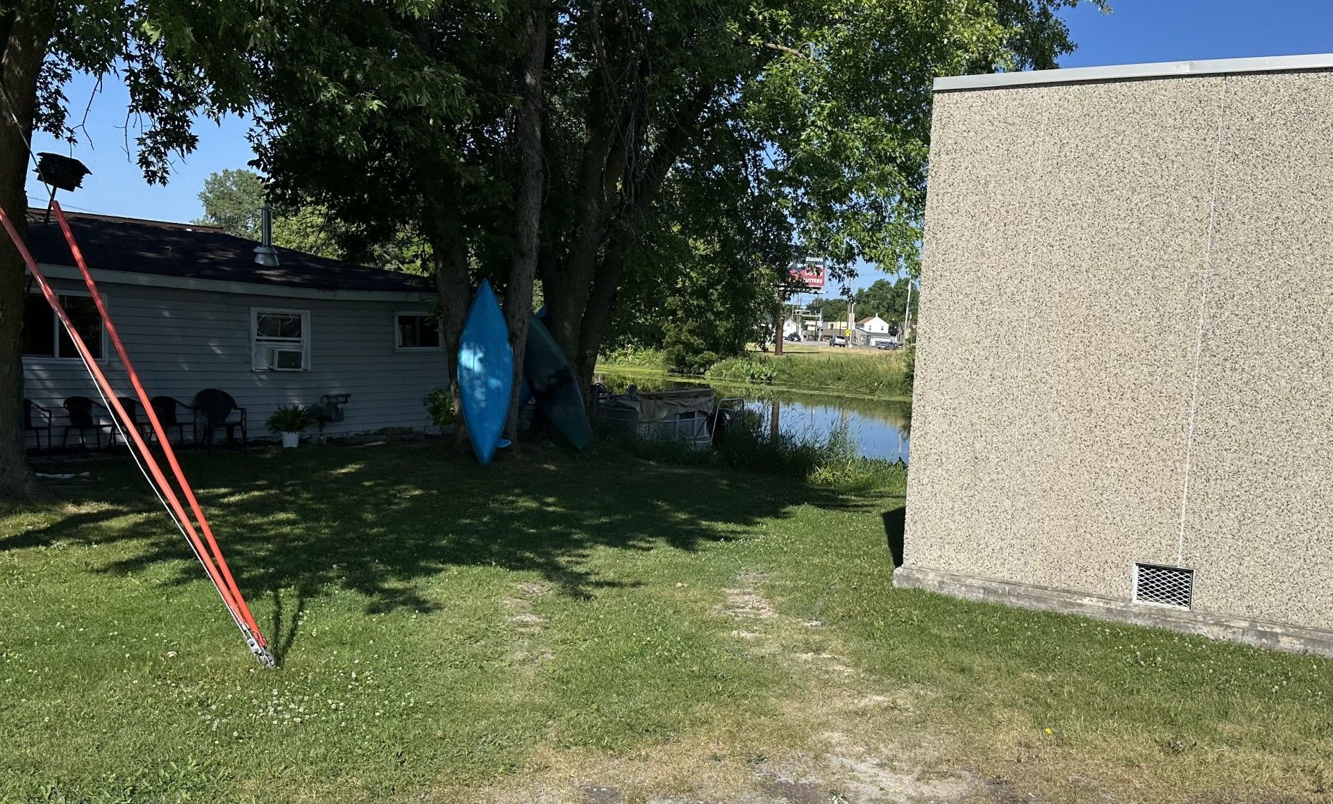 Une zone herbeuse avec une maison, un étang et un bâtiment à l’extérieur texturé.