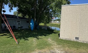 A grassy area with a house, a pond, and a building with a textured exterior.