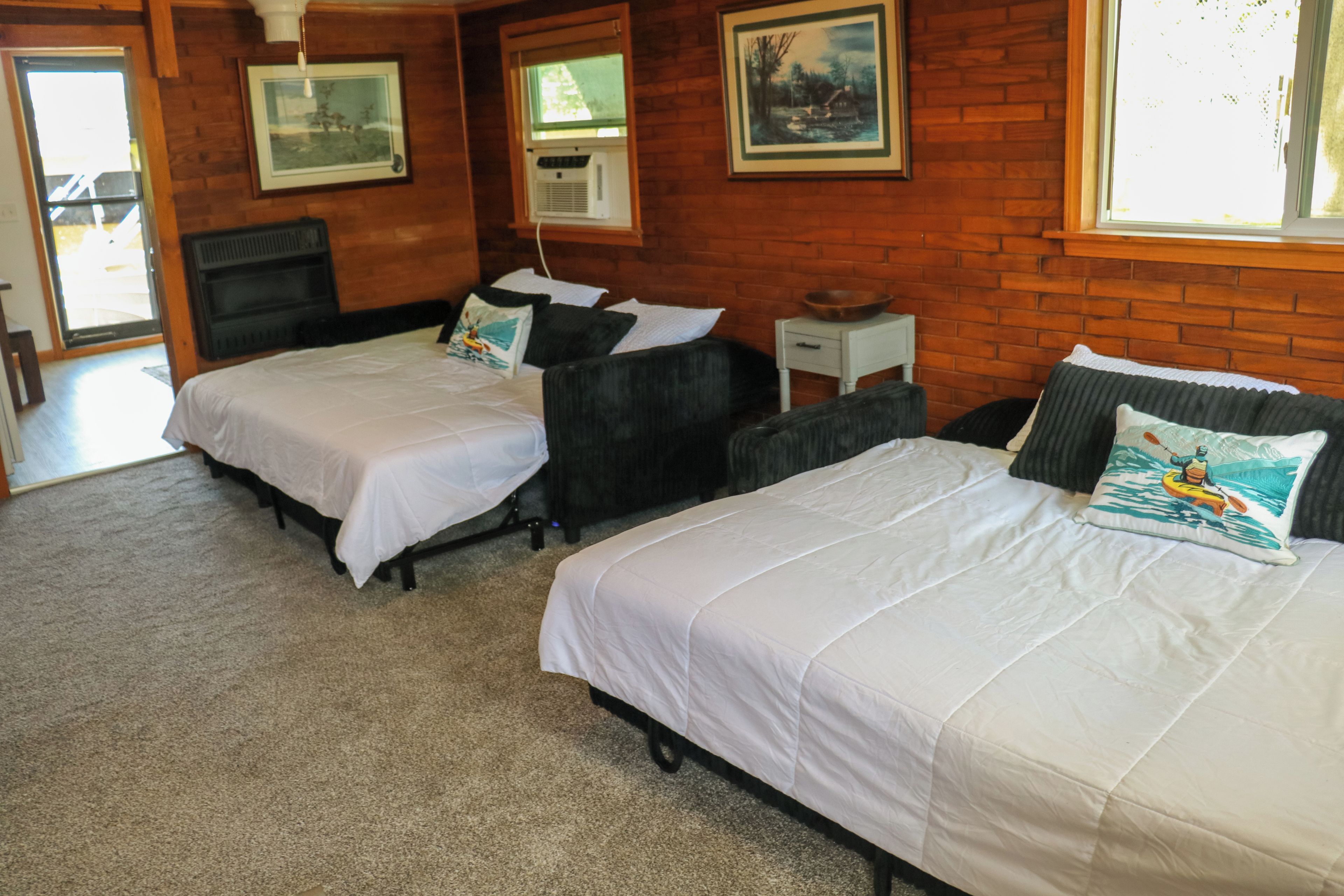 Habitación de hotel con dos camas, una ventana, un calefactor y un cuadro en la pared.