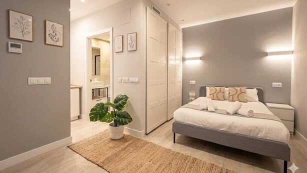 Une chambre à coucher moderne avec un lit, des tables de chevet, une plante en pot et un dressing.