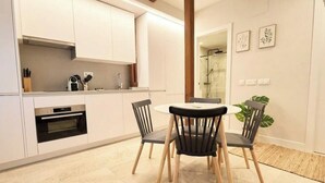 Une cuisine moderne avec des armoires blanches, un four encastré et un coin repas comprenant une table ronde et deux chaises.