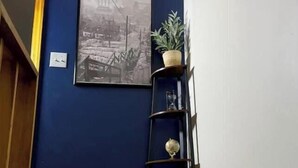 Ein Flur mit dunkelblauer Wand, einem gerahmten Bild, einer Topfpflanze und einem schwarzen Regal mit Dekoration.