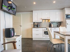 Una cocina moderna con armarios blancos, una mesa de comedor con sillas, una cafetera y un televisor instalado en la pared.