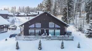 Uma cabana de madeira com uma grande porta de vidro, rodeada por árvores cobertas de neve e um céu limpo.