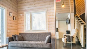 Interior de cabana de tronco moderna, com sofá cinza, escada e área de jantar.