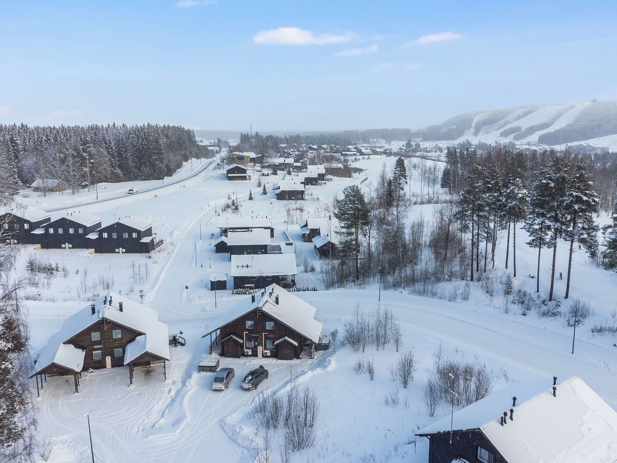 A snow-covered village with wooden buildings, a ski slope, and a clear sky.