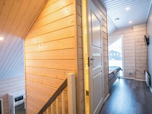 A wooden interior with a staircase, a door leading to another room, and a view of the outside.