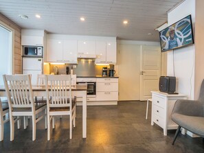 Una cocina moderna con armarios blancos, un microondas y una cafetera. Hay una mesa de comedor con sillas y un sofá gris.