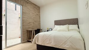 Un dormitorio con cama, una mesita, una silla y una pared de ladrillo.