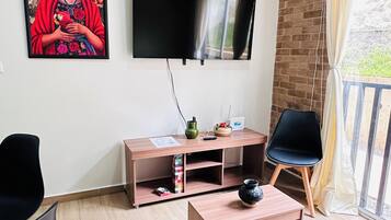 A modern living room with a flat-screen TV, a wooden coffee table, a black sofa, a black armchair, and a colorful painting on the wall.
