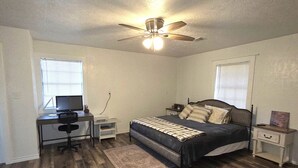 A bedroom with a bed, a desk, a chair, a ceiling fan, and a window.