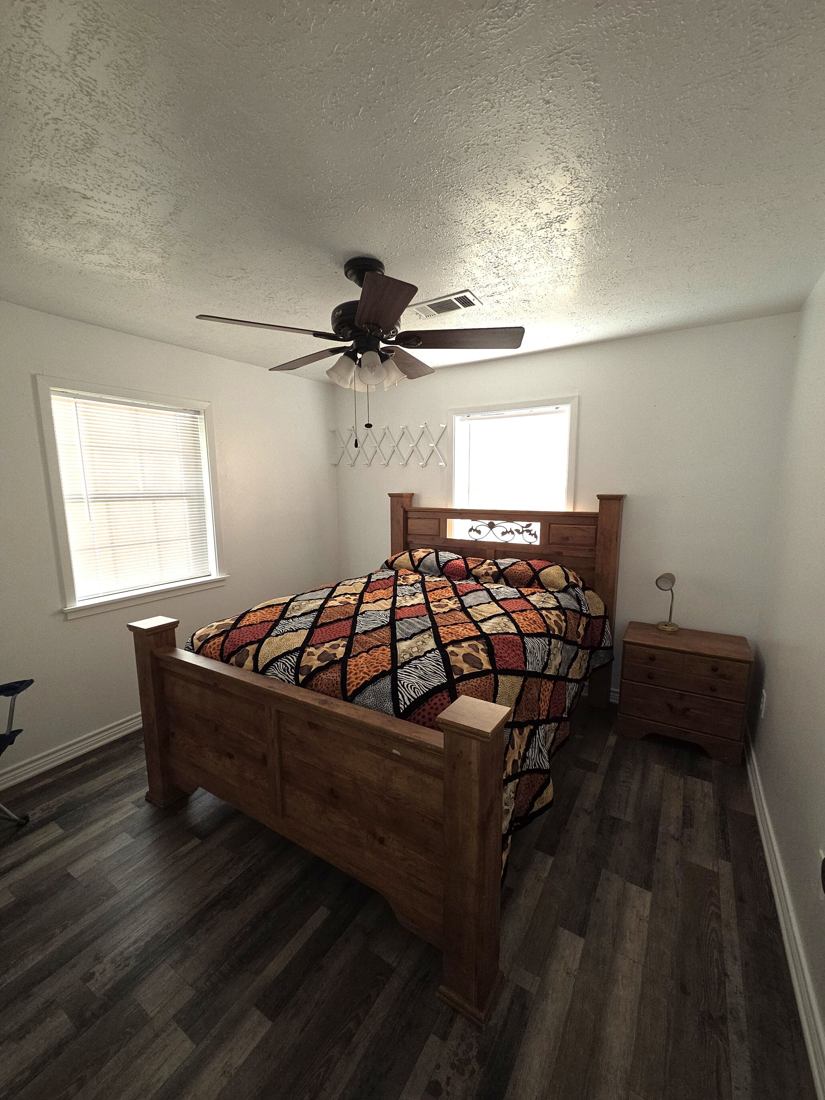 Un dormitorio con cama de madera, ventilador de techo, ventana y mesita de noche.
