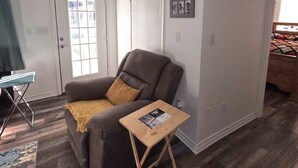 A living room with a brown recliner, a small wooden table, a door with a window, and a framed picture on the wall.