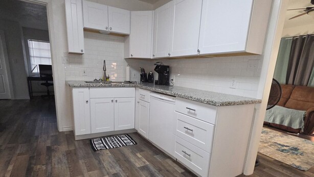 A kitchen with white cabinets, a granite countertop, and a patterned rug.