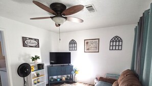 A living room with a ceiling fan, a TV, a sofa, a coffee table, a bookshelf, and a decorative wall.