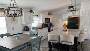 A kitchen with white cabinets, a central island with bar stools, a dining table with chairs, and pendant lighting. - Weeki Wachee 3BR Private Dock, Kayak, Fish & Boat, Trailer Parking, Sleeps 6 (Spring Hill)