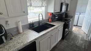 A kitchen with white cabinets, a black sink, a microwave, and a dishwasher. - Weeki Wachee 3BR Private Dock, Kayak, Fish & Boat, Trailer Parking, Sleeps 6 (Spring Hill)