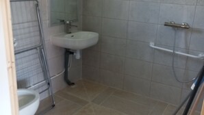 Un baño con inodoro, lavamanos, ducha y cubo de limpieza.