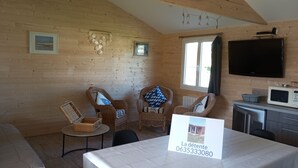 Un interior de madera con sillas de mimbre, una mesa con un cartel, un televisor y un microondas.