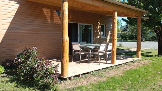 Una cabaña de madera con un porche cubierto, una mesa de comedor y sillas.