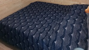 Una habitación con paredes de madera, una ventana con cortina y una cama con colcha estampada.