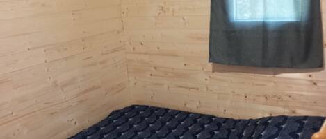 A room with wooden walls, a window with a curtain, and a bed with a patterned bedspread.
