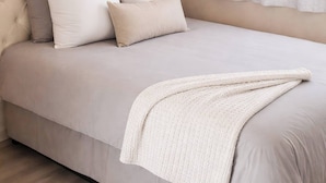 Ein Schlafzimmer mit einer gesteppten Kopfteil, einem Bett mit weißer Bettwäsche, einer weißen Tagesdecke und einem Fenster mit durchsichtigen Vorhängen.