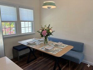 A dining area with a table set for two, a vase of flowers, and a bench.