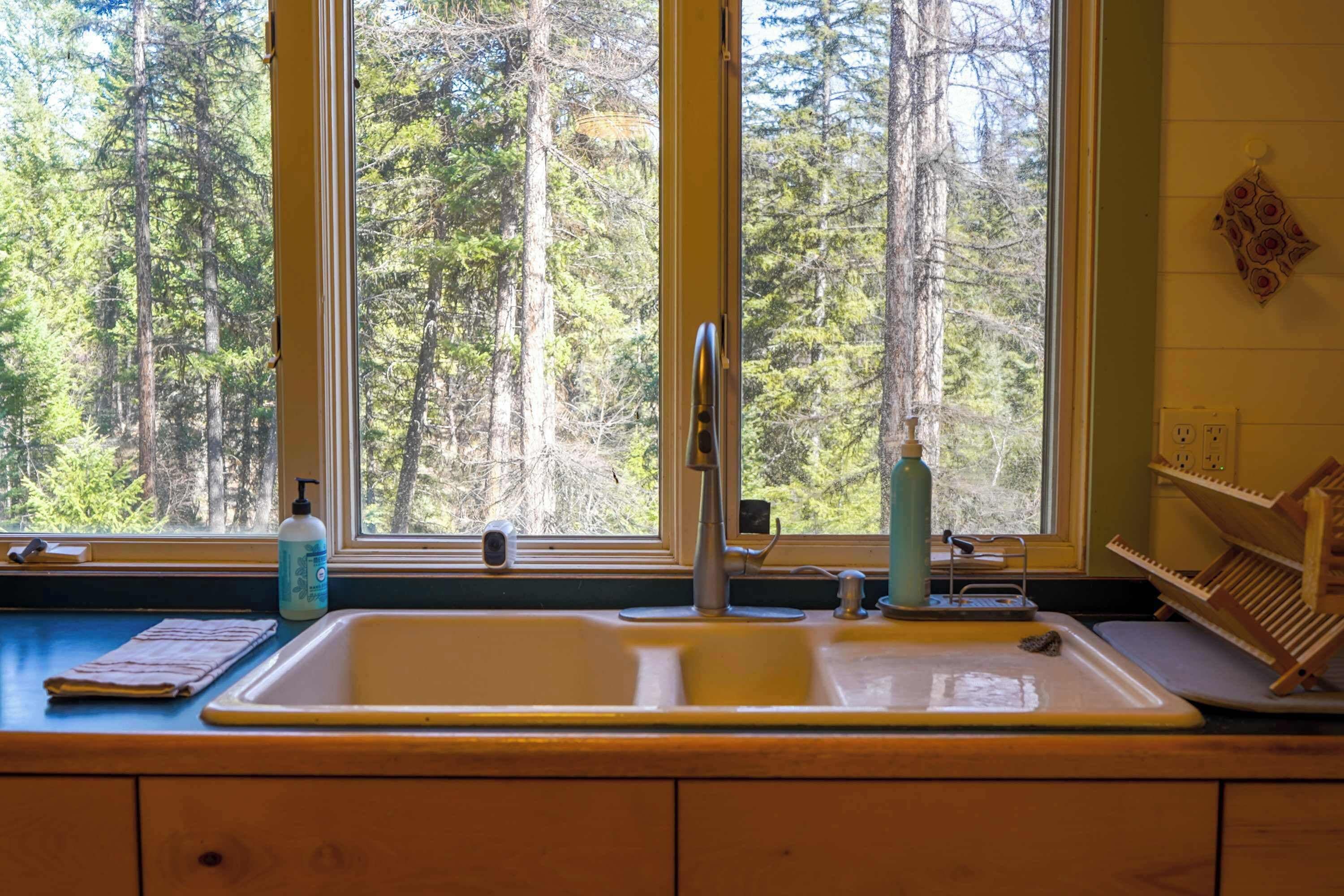 A kitchen with a double sink, a window with a view of trees, and a wooden rack with utensils.