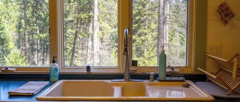 A kitchen with a double sink, a window with a view of trees, and a wooden rack with utensils.