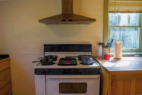 Une cuisine équipée d’une cuisinière, de casseroles, de poêles et d’une fenêtre donnant sur des arbres.