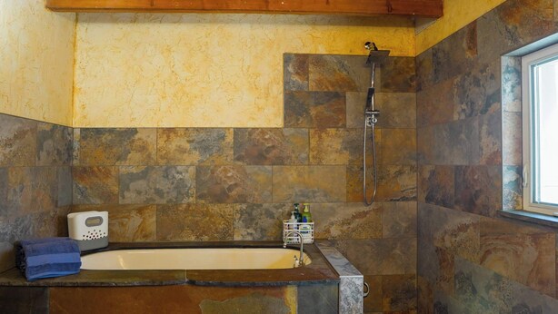 A bathroom with a stone wall, a bathtub, a shower, and a window. - Off Grid Retreat Stay for 7 (Rexford)