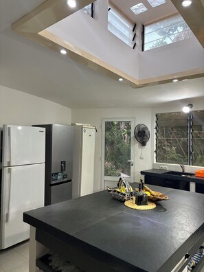 Una cocina moderna con una isla central, dos refrigeradores, un ventanal con vistas a zonas verdes y un tragaluz.