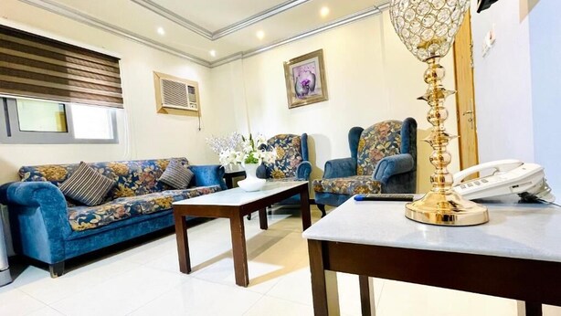 Uma sala de estar com um sofá, duas poltronas, uma mesa de centro, um abajur decorativo e um telefone.