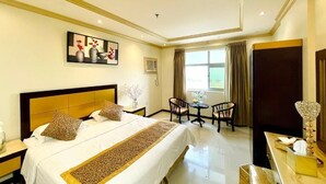 Quarto de hotel com cama, escrivaninha, cadeira, janela com cortinas e um quadro na parede.