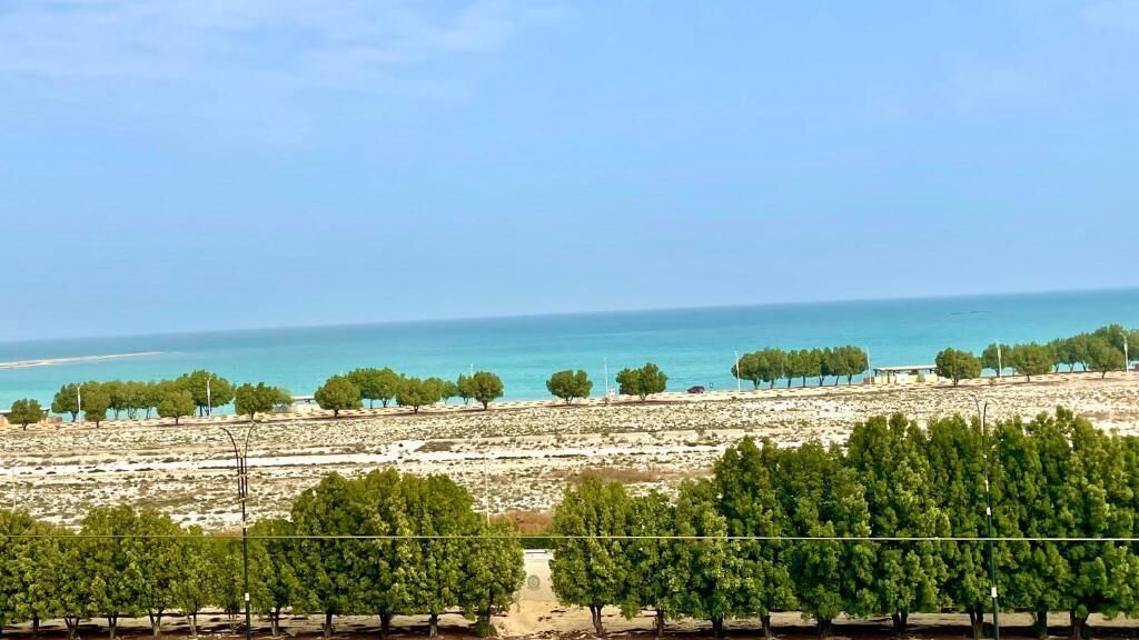 A coastal landscape with a clear sky, trees, and a view of the sea.