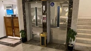 Entrada de hotel com balcão de recepção, sinal de acessibilidade para deficientes e escadas para o andar superior.