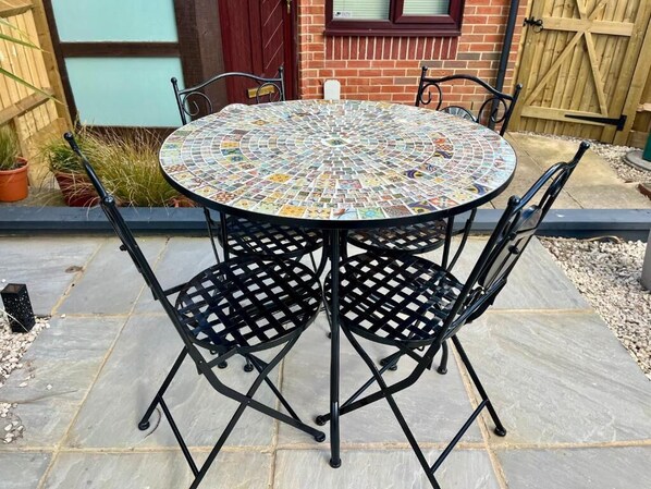 A round outdoor table with a mosaic tabletop surrounded by four black metal chairs.