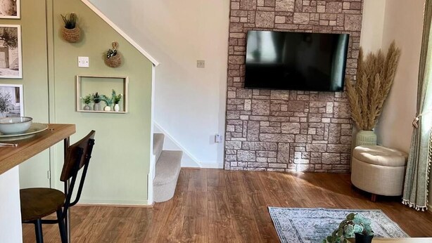 Uma sala de estar com parede de pedra, televisão de tela plana, mesa de jantar de madeira e escada.