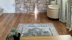 Sala de estar com parede de pedra, televisão de tela plana, piso de madeira, tapete estampado e planta em vaso.