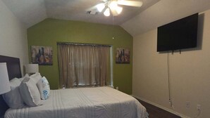 A bedroom with a bed, a ceiling fan, a flat-screen TV, and artwork on the walls. - Hook, Line & Relax – Coastal TX Getaway (Texas City)