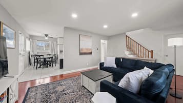A modern living room with a dark blue sofa, a coffee table, a patterned rug, and a staircase leading to an upper level.