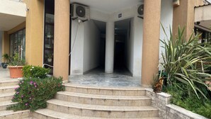 A building entrance with steps leading up to a covered area, air conditioning units, and potted plants. - City Suites Budva  (Budva)