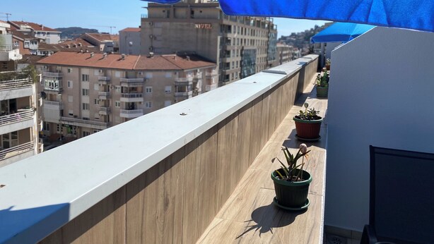 A balcony with a view of buildings, a wooden railing, and potted plants. - City Suites Budva  (Budva)