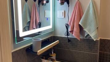 A bathroom with a white sink, a mirror with lights, and towels hanging on hooks.