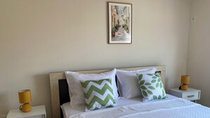 A neatly made bed with white bedding and decorative pillows, a framed artwork above the bed, and two bedside tables with lamps on either side. - City Suites Budva  (Budva)
